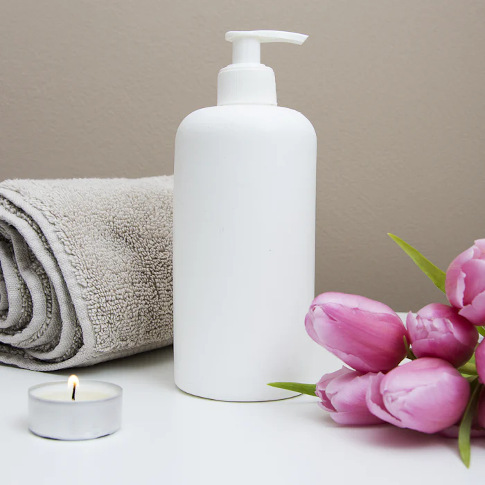 Rolled white towel, a lit candle and pink tulips on a spa table