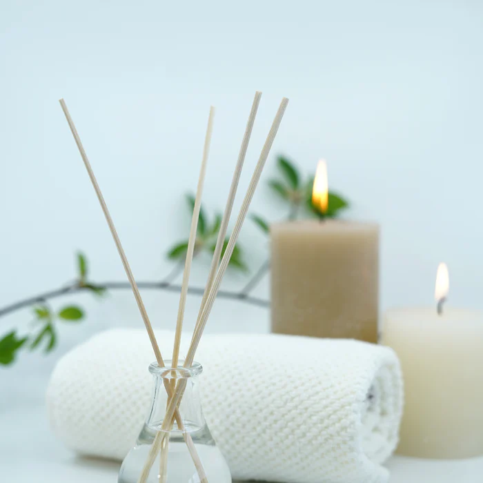 Reed diffuser beside folded white towels and a candle