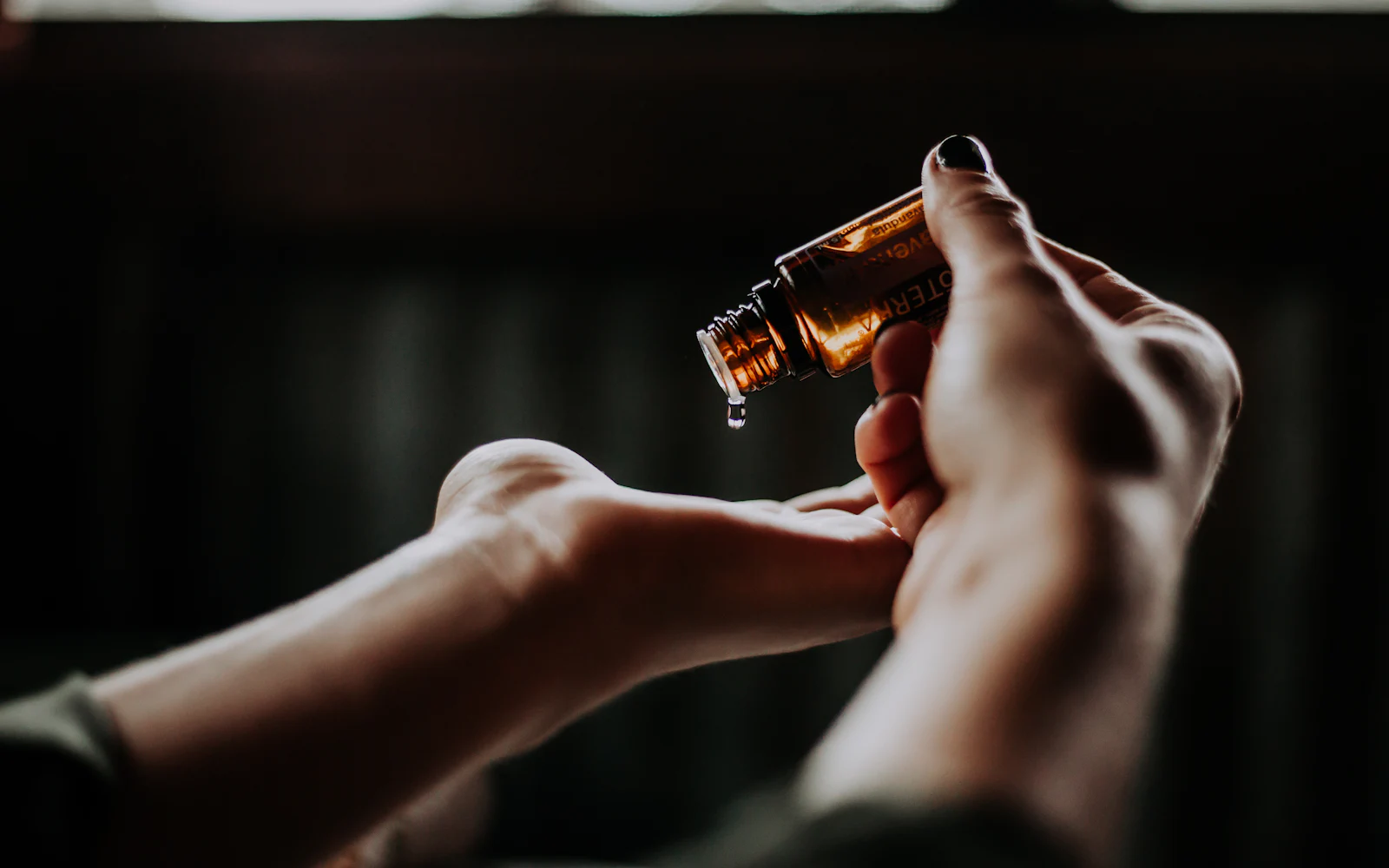 Aromatic massage oil being poured from an amber bottle into an open palm